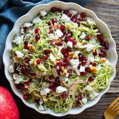 a white bowl filled with shredded cabbage and pomegranates next to an apple