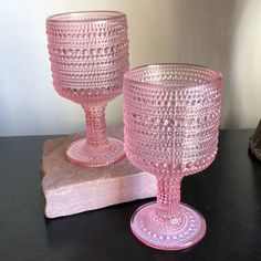 two pink glass goblets sitting on top of a wooden block next to each other