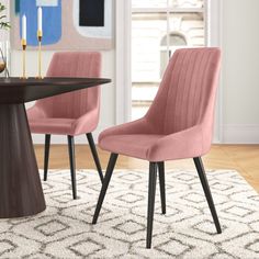 two pink chairs sitting on top of a rug next to a wooden table with candles