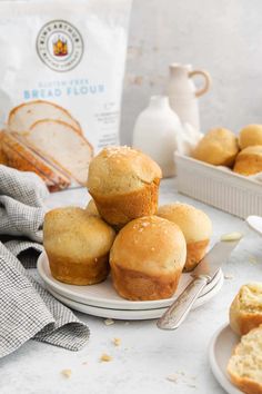 some muffins are stacked on a plate next to a bag of bread and a glass of milk