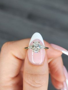 a woman's hand with pink and white manicured nails holding a diamond ring