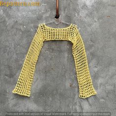 a yellow knitted sweater hanging on a clothes hanger in front of a concrete wall