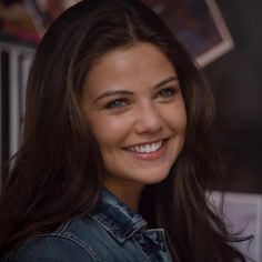 a close up of a person wearing a jean jacket and smiling at the camera with long hair