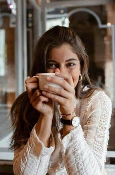 a woman sitting at a table drinking from a cup with her hands on her face