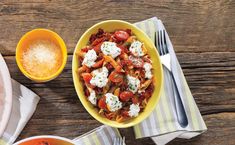 two bowls filled with pasta and sauce on top of a wooden table next to silverware