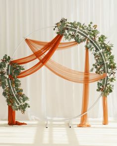 an orange and white wedding arch decorated with greenery