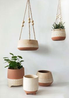 three hanging planters with plants in them, one is white and the other has brown