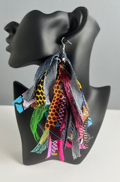 a black mannequin head is adorned with multicolored fabric and metal earrings