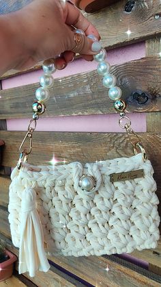 a hand holding a white purse on top of a wooden bench