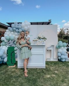 a woman standing in front of a table with balloons on it and a baby sitting on her lap