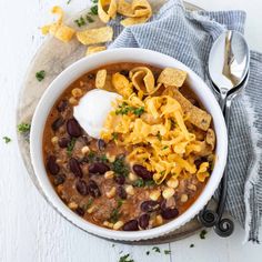 a bowl of chili with tortilla chips and sour cream on top, next to a spoon