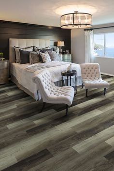 a bedroom with wood flooring and white bed in the center, two chairs on either side