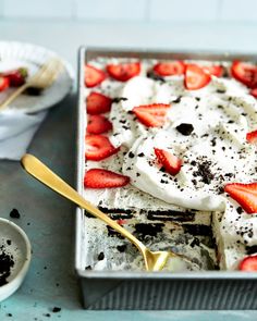 a dessert with strawberries and cream in a pan on a table next to a bowl of chocolate chips