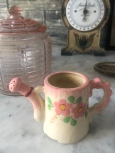 a pink flowered coffee cup sitting on top of a counter next to a clock