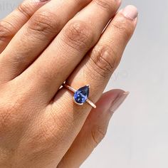 a woman's hand holding a blue ring with a diamond on it and the middle finger