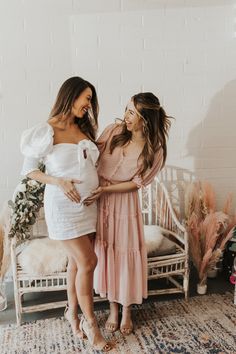 two women standing next to each other in front of a white wall