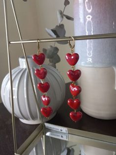 a pair of red heart shaped earrings hanging from hooks on a shelf next to a white vase