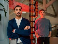 two men standing next to each other in front of a tall sculpture with red lights on it