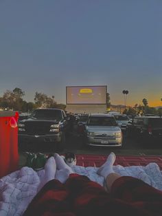 a person laying on a blanket in front of a movie screen with cars parked behind them