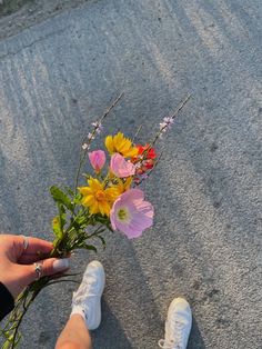 a person holding flowers in their hand on the ground next to someone's feet