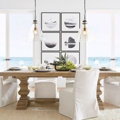 a dining room table with white chairs and pictures on the wall above it, along with an ocean view