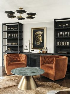 a living room with two chairs and a table in front of shelves filled with glasses