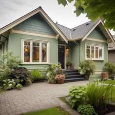 a green house with lots of plants in the front yard and steps leading up to it