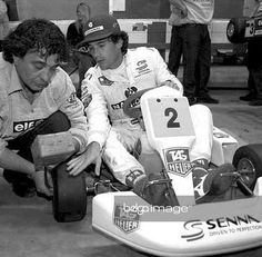 two men sitting on top of a race car in front of another man holding the steering wheel