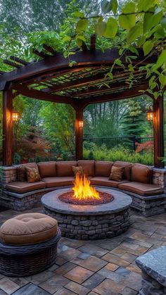 an outdoor fire pit surrounded by seating and greenery with lights on the ceiling above it