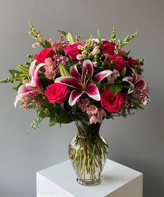 a vase filled with pink and red flowers on top of a white table next to a gray wall