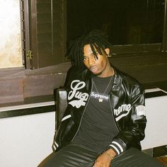 a man with dreadlocks sitting in a chair wearing a black shirt and leather pants