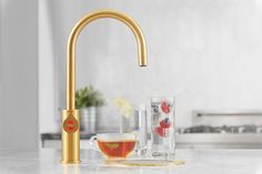 a gold faucet on a kitchen counter with ice and fruit in the bowl