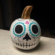 a white pumpkin decorated with blue and pink sugar skull decorations on top of a counter