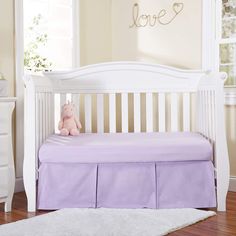 a white crib with a pink teddy bear sitting on it's bed skirt