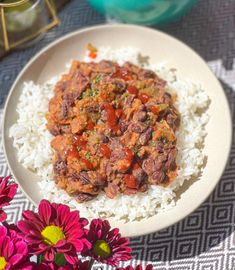 a white plate topped with rice and meat on top of a table next to flowers