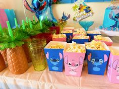 the table is set up with many cups and containers filled with popcorn, including one that has an image of stitch on it