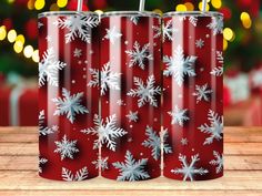 two red tumblers with silver snowflakes are on a wooden table in front of a christmas tree