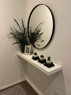 there is a mirror and some plants on the shelf in the corner by the wall