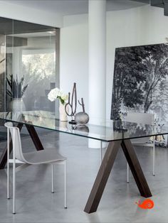 a glass table with two chairs and a painting on the wall in front of it