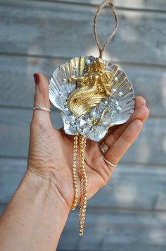 a hand holding an ornament shaped like a shell with a gold mermaid on it