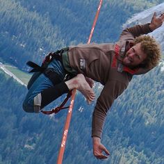 a man on a rope high up in the air with trees and mountains behind him