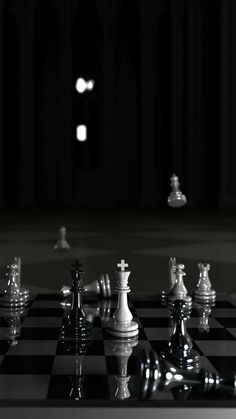 a black and white photo of chess pieces on a checkerboard floor with lights in the background