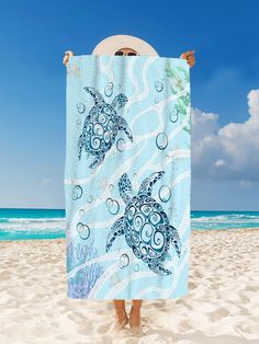 a woman holding up a towel with a sea turtle design on it at the beach