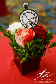 an arrangement of roses and greenery in a vase on a red table cloth covered table