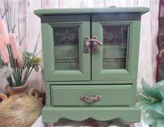 a green cabinet sitting next to a vase with flowers in it on top of a table