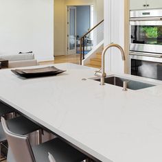 a modern kitchen with stainless steel appliances and white countertops, along with black chairs