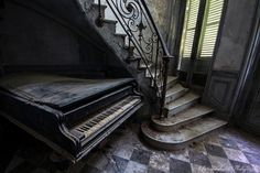 an old piano sitting in the corner of a room next to a stair case and window