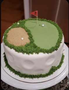 a cake decorated with green grass and a golf hole on the top is white icing