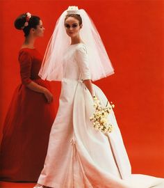 two women in wedding gowns standing next to each other, one wearing a veil