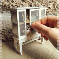 a hand is holding a miniature white birdcage